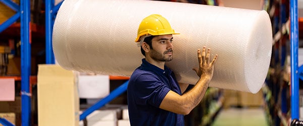 person carrying a large roll of bubble wrap at the warehouse