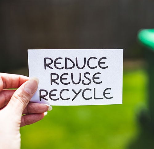 person holding a card says reduce, reuse and recycle