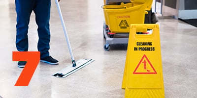 A custodian mopping floor with cleaning cart and wet floor sign