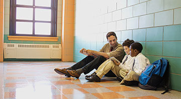 a teacher and two kids sitting in a school hallway hard floor