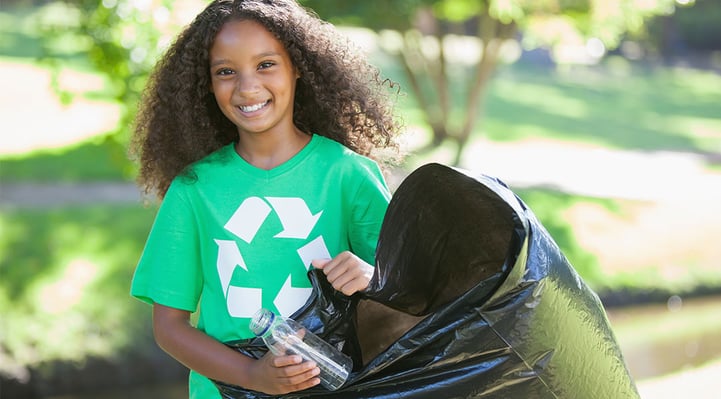 a girl wearing green shirt with recycling symbol collecting plastic bottle for recycle trash bag