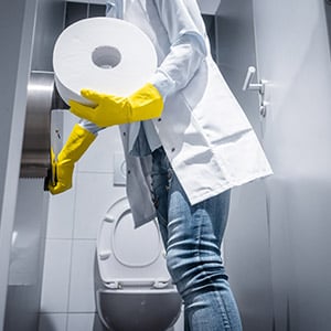 custodian replacing restroom toliet paper on a dispenser