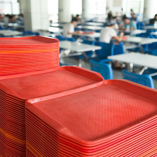 school cafeteria with stacks of red lunch trays with students eating lunch in the background