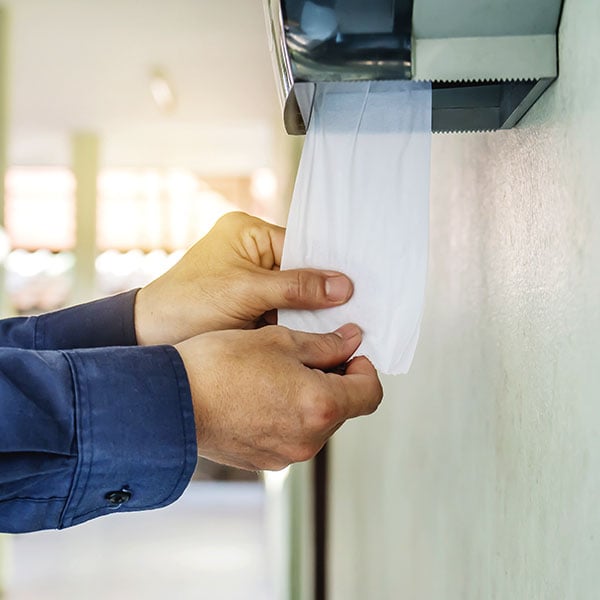 a person's hand pulling paper towel out of dispenser in a restroom