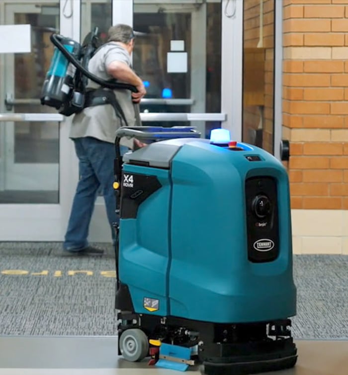 a school custodian cleaning while autonomous floor cleaner cleaning the floor