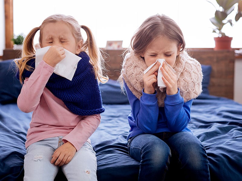 two kids blowing their noses - sick students with cold & flu